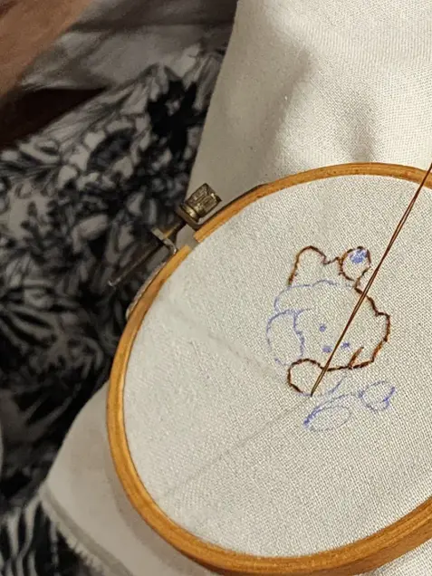 A teddy bear outline stitched in brown thread in a wooden embroidery hoop
