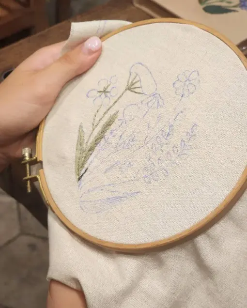 An embroidery hoop with a flower design part stitched in green thread