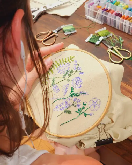 A guest stitches blue and purple wildflowers in an embroidery hoop on the worktable