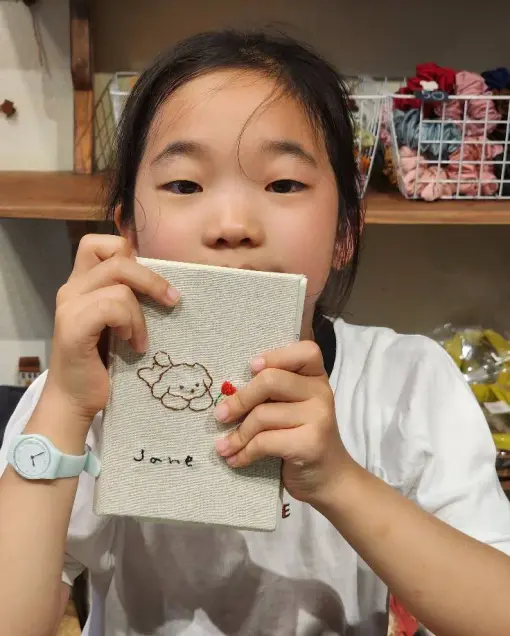 A child shows a notebook with a puppy embroidered on its fabric cover