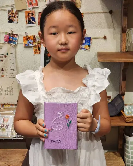A child holds a purple notebook with a swan embroidered on the cover
