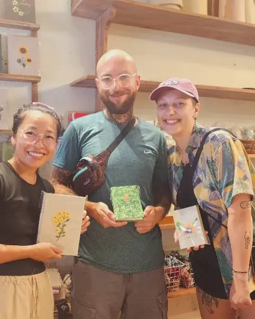 Three people show notebooks with embroidered flower covers after the workshop