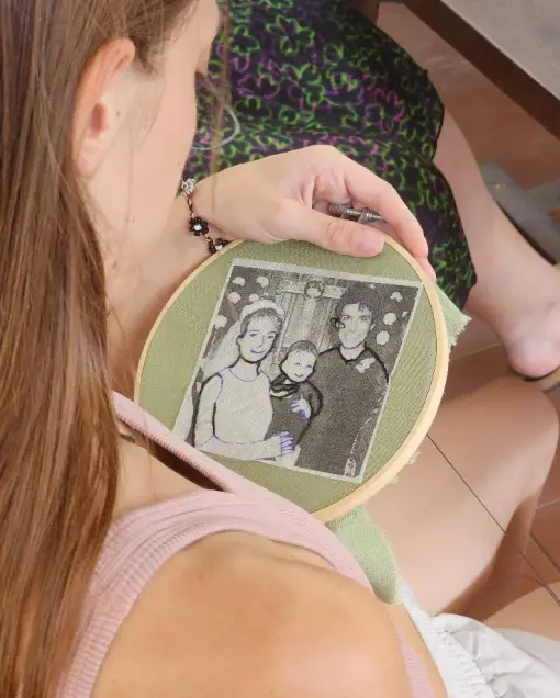A guest holds a hoop with a family portrait on green fabric, ready to embroider