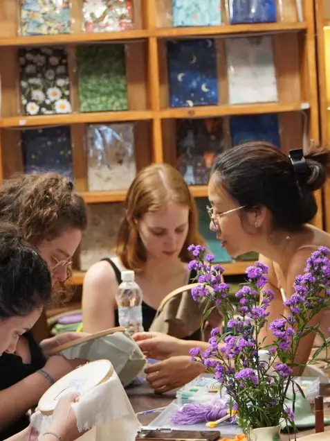 Guests embroider together at a table with fresh purple flowers