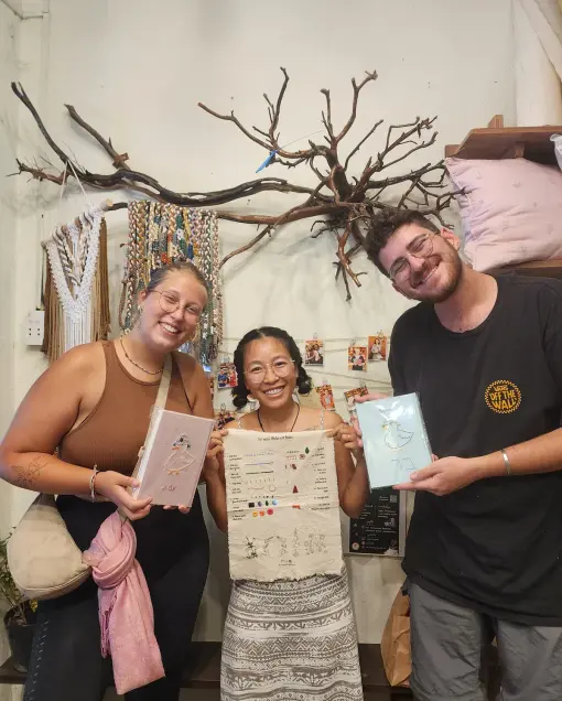 Three people show finished embroidered notebooks and a stitch sampler