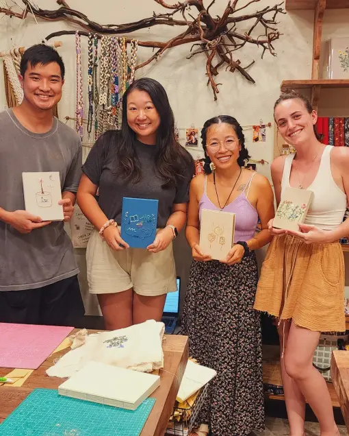 Four people hold handmade notebooks at the bookbinding table