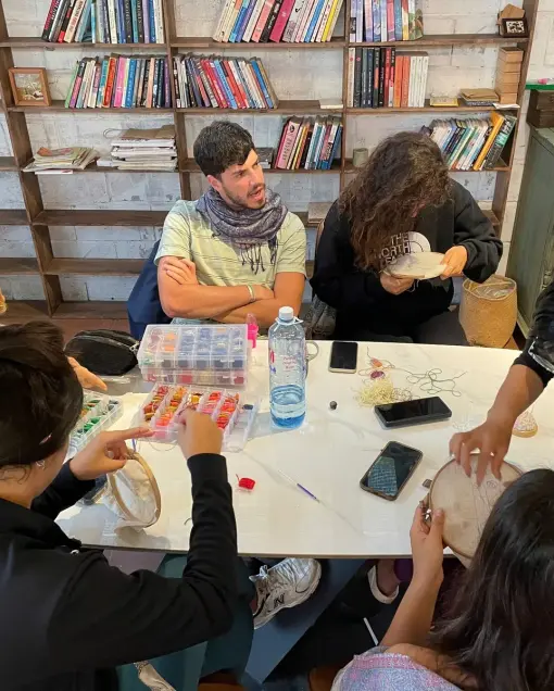 A group embroiders around a table with thread boxes, in front of bookshelves