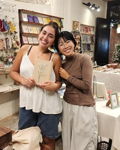 Two people smile with an embroidered notebook in the craft shop