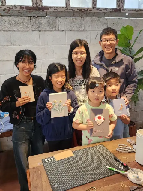 A family shows the embroidered notebooks they made together