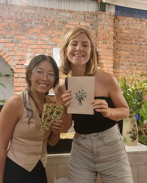 Two guests hold notebooks with embroidered plant designs