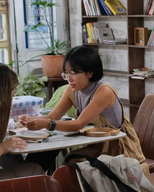 A guest gets help with a stitch at a round table