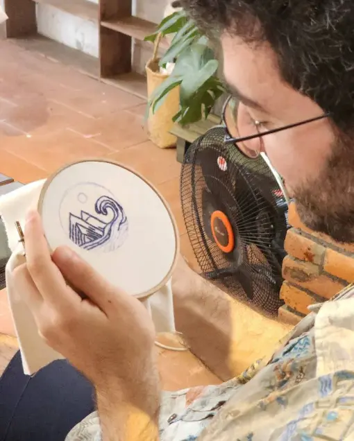 A guest embroiders a blue wave design in a hoop